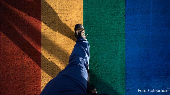 IDAHOBIT Eine Person geht über eine asphaltierte Straße, die in den Regenbogenfarben angemalt ist.